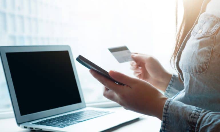 woman on phone and laptop entering her credit card information